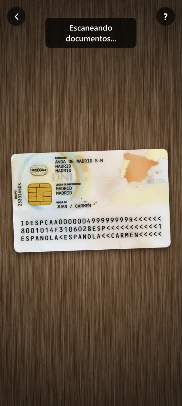 Móvil sostenido en vertical con la cámara abierta. El mismo DNI se ve, pero solo ocupa el tercio central de la pantalla, con mesa vacía arriba y abajo. Texto sobreimpreso: "Escaneando documentos..."