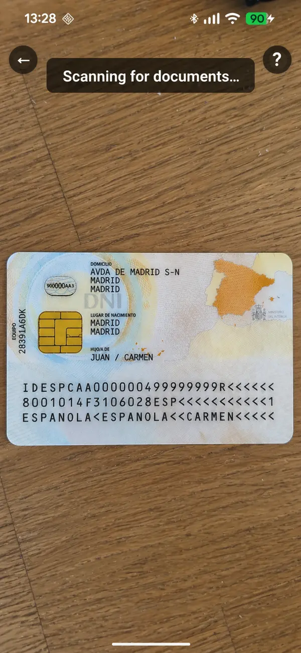 Phone held upright with the camera open. The same ID card is visible but only fills the middle third of the screen, with empty desk above and below. Caption overlay: "Scanning for documents…"